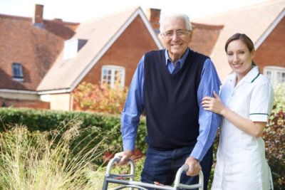 caregiver helps senior man to walk in garden using walking frame